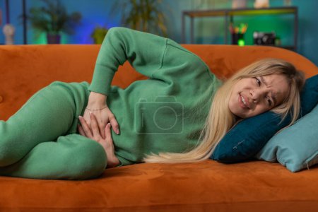 Photo for Sick ill woman suffering from period cramps, painful stomach ache lying on sofa at home room. Girl holding belly, feeling abdominal or menstrual pain. Abdominal pain, gastritis, diarrhea, indigestion - Royalty Free Image