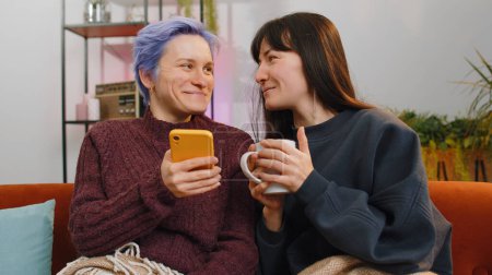 Foto de Dos mujeres alegres, lesbianas o amigos, utilizan teléfonos inteligentes para ir de compras en las plataformas de comercio electrónico en la sala de estar en casa, experimentando diversión, diversión mientras navegan por varias aplicaciones de redes sociales juntos - Imagen libre de derechos