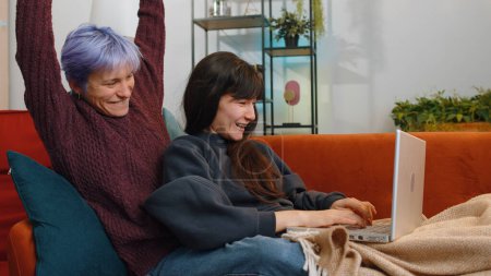 Photo for Two lesbian women family couple friends with laptop scream in delight clapping hands in triumph gesture celebrate success win money in lottery at home living room. Excited girls get online good news - Royalty Free Image