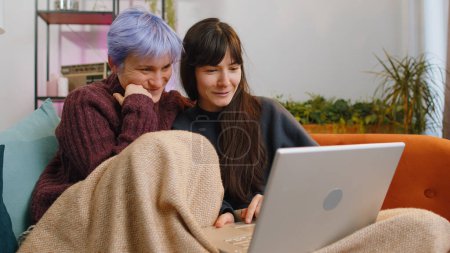Photo for Two lesbian women couple or girls friends looking at laptop camera, making video webcam conference call with family, enjoying pleasant conversation, laughing, waving hello at home room. LGBT people - Royalty Free Image