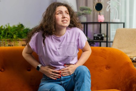 Photo for Sick ill woman suffering from painful stomach ache, period cramps lying on sofa at home room. Girl holding belly, feeling abdominal or menstrual pain. Abdominal pain, gastritis, diarrhea, indigestion - Royalty Free Image