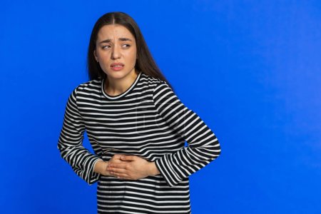 Sick ill woman in striped blouse suffering from period cramps, painful stomach ache. Girl holding belly feeling abdominal or menstrual pain. Abdominal pain gastritis diarrhea indigestion. Copy-space