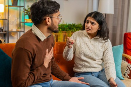 Upset young Hispanic couple in casual clothes arguing fighting while sitting on sofa in living room at home. Diverse disappointed girlfriend and boyfriend shouting at each other on couch in apartment.