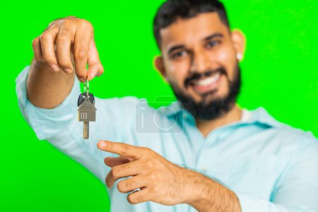 Téléchargez les photos : Jeune homme indien agent immobilier levant la main montrant les clés de l'appartement maison neuve, l'achat ou la location de biens, prêt hypothécaire, assurance. Arabe gars isolé sur fond vert chroma clé - en image libre de droit