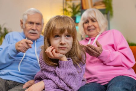 Irritated senior grandfather and grandmother scolding granddaughter for bad behavior and disobedience on sofa, raising voice, scream at little grandchild. Difficulties of upbringing, misbehaved child