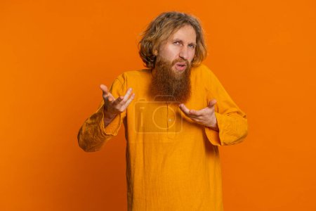 What. Why. Angry Caucasian man raising hands in indignant expression, asking reason of failure, demonstrating disbelief irritation by troubles. Redhead young guy isolated on orange studio background