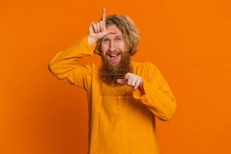 Caucasian man showing loser gesture and pointing on you, blaming accusing for unsuccess, expressing disrespect, mocking your failure, bullying abuse. Young guy isolated on orange background indoors