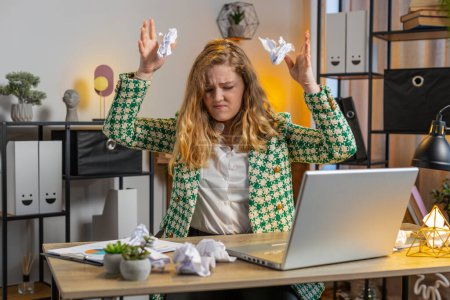 Angry furious Caucasian businesswoman throwing crumpled paper nervous breakdown at work stress management mental distress problems losing temper reaction on failure. Girl sits at home office at desk.