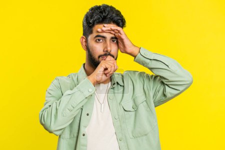 Sad young Indian man feeling hopelessness loneliness, nervous breakdown, loses becoming surprised by lottery results, bad fortune, loss unlucky news. Attractive Hindu guy isolated on yellow background