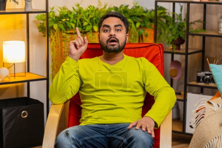 Eureka. Thoughtful clever inspired Indian man make gesture raises finger came up with creative plan feels excited with good idea inspiration motivation question at home apartment. Guy sits on chair