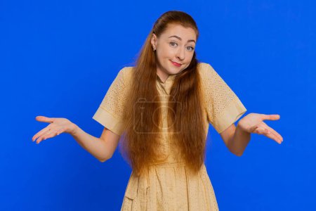 What Why. Sincere irritated young woman raising hands in indignant expression, ask reason of failure demonstrating disbelief irritation by trouble. Confused redhead girl on blue background, indoors