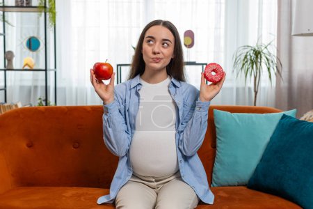 Choosing right nutrition. Confused young pregnant woman comparing sweet donut and ripe apple and shrugging shoulders in uncertainty. Future mother girl hesitates choosing between dessert and fruit.