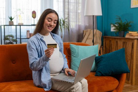Photo for Online shopping, buying from home. Happy pregnant woman sitting on sofa couch and making purchase from online store using laptop and credit card. Happy future mother satisfied with online shopping. - Royalty Free Image