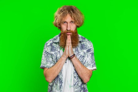 Please, God help. Caucasian man praying looking at camera and making wish, asking with hopeful imploring expression, begging apology, meditation. Redhead guy isolated on green chroma key background