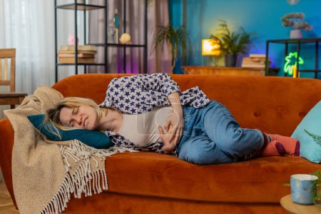 Photo for Upset young woman embracing belly suffering from stomachache lying on sofa. Unhappy sad Caucasian girl having menstrual painful feelings, resting on couch. Gastritis, abdominal or period pain concept. - Royalty Free Image