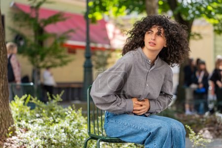 Photo for Sick ill young woman suffering from period cramps painful stomach ache outdoors. Girl holding belly feeling abdominal menstrual pain sitting on urban city street. Abdominal pain gastritis. Sunny park - Royalty Free Image