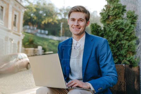 Téléchargez les photos : Freelancer jeune homme d'affaires en costume de travail sur ordinateur portable assis à l'extérieur. - en image libre de droit
