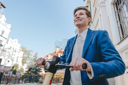 Photo for Young man wearing suit riding on electric scooter on the city street. Selective focus. - Royalty Free Image