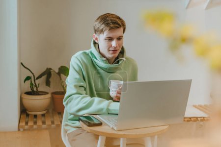 Photo for Freelancer young man working on laptop sitting in the cafe with cup of coffee. Selective focus. - Royalty Free Image