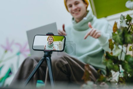 Téléchargez les photos : Jeune blogueur homme faisant vlog en utilisant smartphone assis en plein air. Concentration sélective. - en image libre de droit