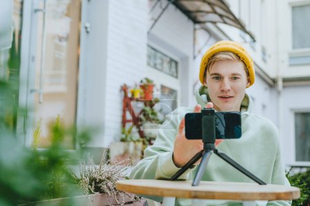 Photo for Young man blogger making vlog using smartphone sitting outdoor. Selective focus. - Royalty Free Image