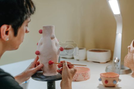 Foto de Primer plano de la joven alfarera decorando un jarrón hecho a mano en el taller. Enfoque selectivo. - Imagen libre de derechos