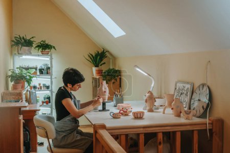Photo for Young woman craft person potter painting a vase sitting at her workshop. Selective focus. - Royalty Free Image