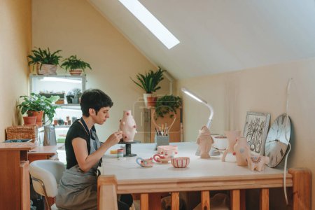 Téléchargez les photos : Jeune femme peignant un vase assis à la table de l'atelier. Concentration sélective. - en image libre de droit