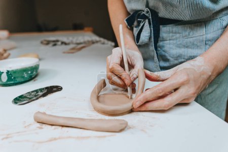 Téléchargez les photos : Jeune femme potier travaillant avec de l'argile dans un atelier. Gros plan des mains féminines. Concentration sélective. - en image libre de droit