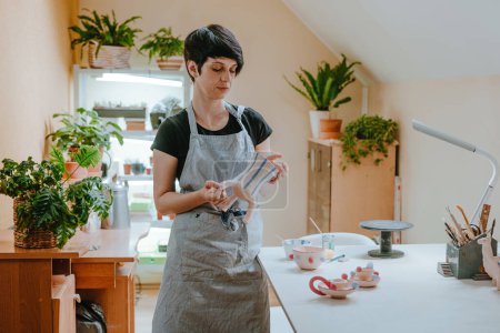 Téléchargez les photos : Jeune femme artisan potier tenant un vase debout dans l'atelier. Concentration sélective. - en image libre de droit