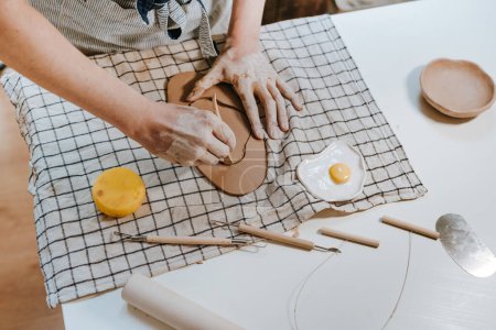 Téléchargez les photos : Jeune femme potier sculptant une assiette d'argile dans son atelier. Gros plan des mains féminines. Concentration sélective. - en image libre de droit