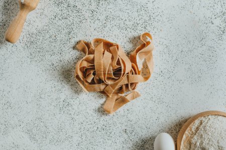 Photo for Handmade pasta in the shape of a nest on a white table surrounded by a rolling pin, flour and eggs. Top view, flat lay. Selective focus. - Royalty Free Image