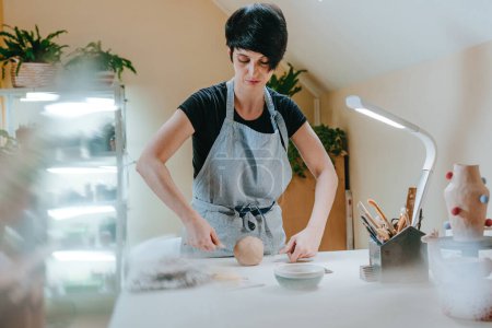 Téléchargez les photos : Femme artisan potier argile de coupe avec un outil spécial à l'atelier. Concentration sélective. - en image libre de droit