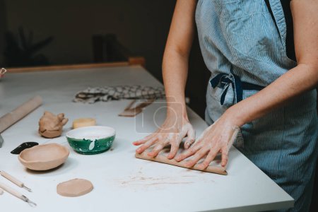 Téléchargez les photos : Jeune femme potier travaillant avec de l'argile rouler dans un atelier. Gros plan des mains féminines. Concentration sélective. - en image libre de droit
