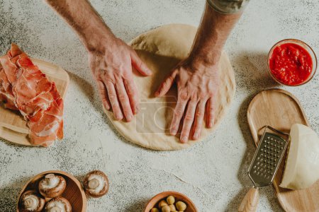 Photo for Close-up of man preparing pizza on a white table. Ingredients near dough. Top view, flat lay. Selective focus. - Royalty Free Image