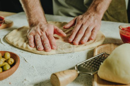 Photo for Close-up of man preparing pizza on a white table. Ingredients near dough. Selective focus. - Royalty Free Image