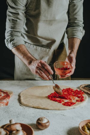 Photo for Close-up of man preparing pizza on a white table against black background. Selective focus. - Royalty Free Image