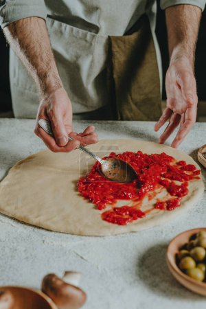 Photo for Close-up of chef preparing pizza putting tomato sauce on the dough. Selective focus. - Royalty Free Image