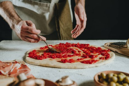 Photo for Close-up of chef preparing pizza putting tomato sauce on the dough. Selective focus. - Royalty Free Image