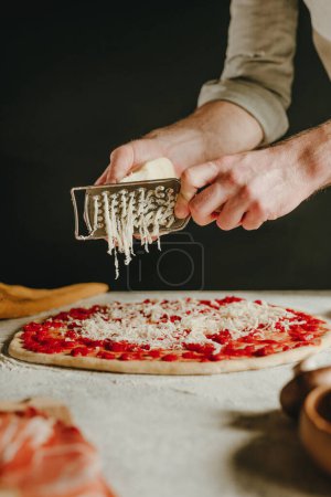 Photo for Close-up of chef preparing pizza grating cheese with a grater on the dough. Selective focus. - Royalty Free Image