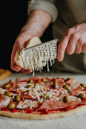 Foto de Chef irreconocible rallando queso sobre una base de pizza en la mesa de la cocina. Primer plano, enfoque selectivo. - Imagen libre de derechos