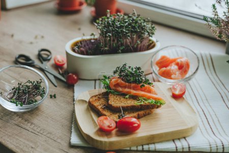 Foto de Sandwich con pan integral, salmón, brotes de rábano microverde, tomate sobre fondo de madera. Enfoque selectivo. - Imagen libre de derechos