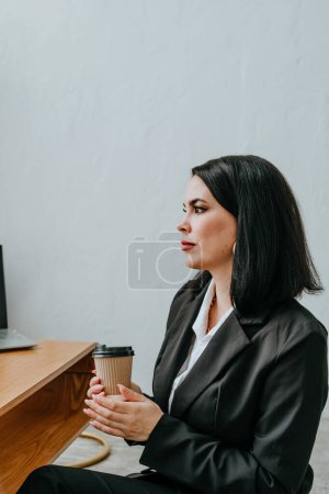 Téléchargez les photos : Une jeune femme en costume d'affaires tenant une tasse de café parle au bureau. Concentration sélective. - en image libre de droit