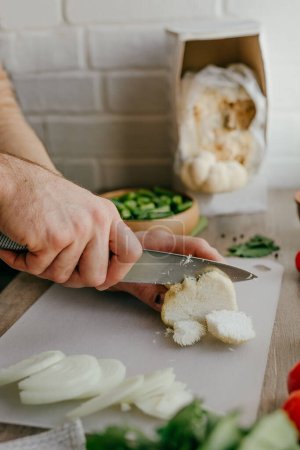 Großaufnahme von männlichen Händen, die mit einem Messer Hericium erinaceus Pilze kochen, die in der Küche gezüchtet werden. Hausgemachte Löwenmähne Pilz wächst zu Hause. Fungikultur und Heimgartenkonzept. Selektiver Fokus.