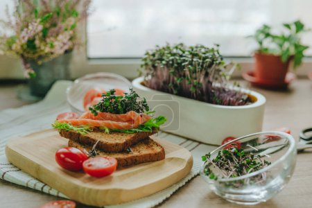 Photo for Sandwich with whole wheat bread, salmon fish, radish sprouts microgreen, tomato on wooden background. Selective focus. - Royalty Free Image