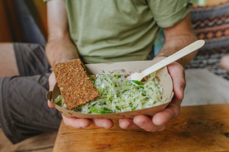Foto de Primer plano de un joven sosteniendo un almuerzo saludable. Ensalada de verduras en un contenedor de almuerzo de papel artesanal. - Imagen libre de derechos
