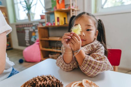 Photo for Girl playing on the table with a feather and natural toys in kindergarten. Selective focus. - Royalty Free Image