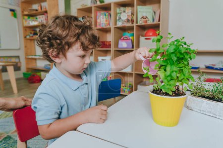 Téléchargez les photos : Garçon arrosant une plante à partir d'un arrosoir de jouet dans une maternelle. Concentration sélective. - en image libre de droit