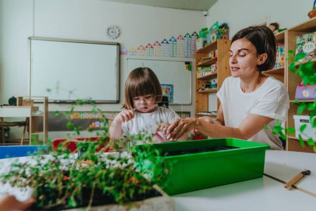 Foto de Joven maestra con niño cuidando plantas en macetas en el jardín de infantes. Enfoque selectivo. - Imagen libre de derechos