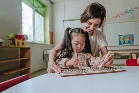 Photo for Girl and teacher playing with educational wooden toys developing coordination with tabletop labyrinths in a kindergarten. Selective focus. - Royalty Free Image
